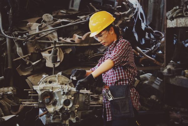 A mechanic fixes an engine while wearing a yellow hard hat and safety glasses.
